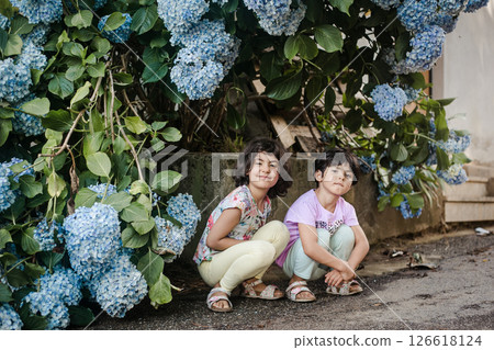 two small girls sitting in front of huge blue hydrangea flowers 126618124