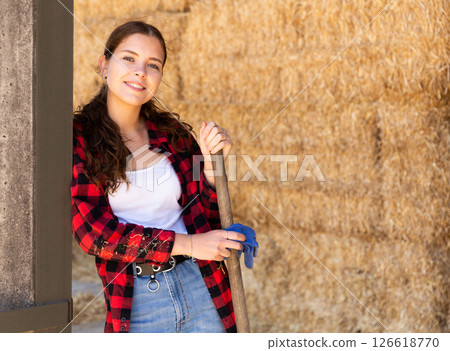 Portrait of a young positive farmer girl standing near haystacks 126618770