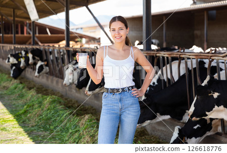 Cheerful young girl with glass of milk near stalls with cows 126618776