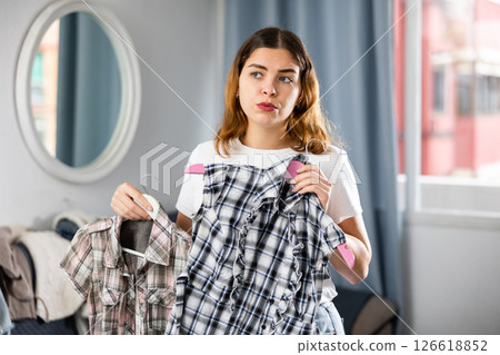 Young woman choosing right shirt to wear Young woman choosing right shirt to wear 126618852
