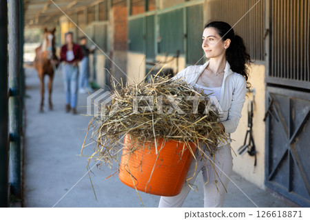 Armenian young female worker walks go through corridor of stable, carrying basket with straw Armenian young female worker walks go through corridor of stable, carrying basket with straw 126618871