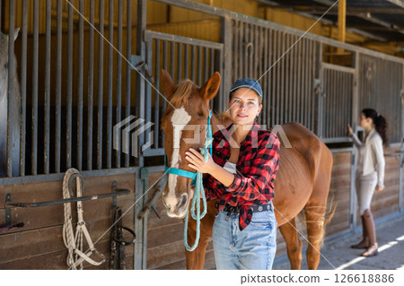 Young woman leads horse out of stable 126618886