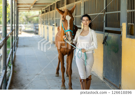 Young woman leads horse out of stable 126618896