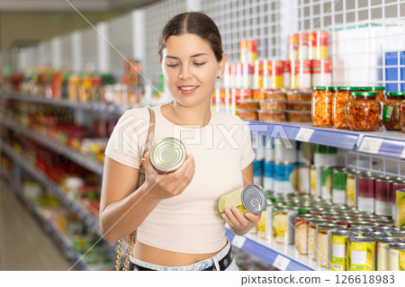 Girl choosing canned Asian vegetables in tin cans in store 126618983