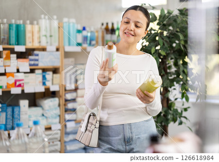Middle-aged woman choosing shampoo or gel in drugstore Middle-aged woman choosing shampoo or gel in drugstore 126618984