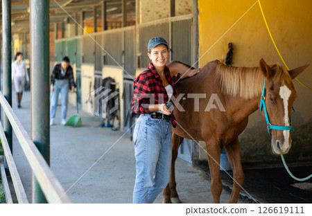 European girl has tied horse to hitching post and is combing animals croup 126619111