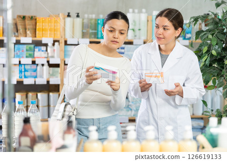 Portrait of young woman pharmacist helping asian female client choosing pill box and making decisions about pharmaceuticals and health care at pharmacy Portrait of young woman pharmacist helping asian female client choosing pill box and making decisions about pharmaceuticals and health care at pharmacy 126619133