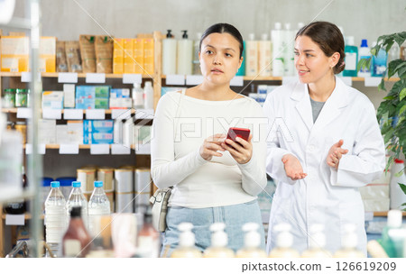 Middle-aged woman scrolling phone while looking for something and pharmacist consulting Middle-aged woman scrolling phone while looking for something and pharmacist consulting 126619209