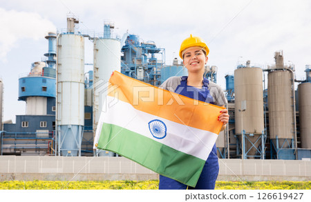 National flag of India in the hands of girl in overalls against background of modern metallurgical plant 126619427