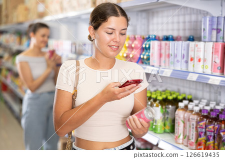 Interested girl scanning QR code on soda can in supermarket 126619435