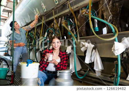 Young female worker standing near milking line with glass of milk Young female worker standing near milking line with glass of milk 126619482