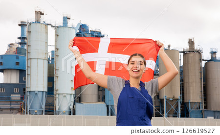 Happy young woman worker with flag of Denmark against background of factory Happy young woman worker with flag of Denmark against background of factory 126619527
