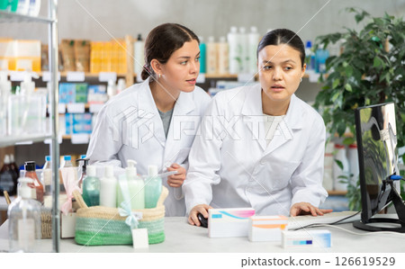 Two pharmacists working with computer in chemist's shop 126619529