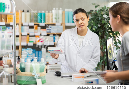 Middle-aged Asian pharmacist offering medicament to client in chemistry Middle-aged Asian pharmacist offering medicament to client in chemistry 126619530