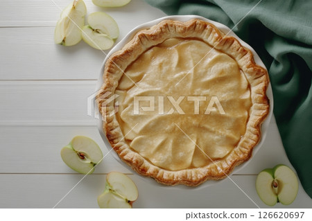 Homemade apple pie with golden crust on white wooden table, surrounded by fresh apple slices and green fabric. Ideal for food blogs, bakery ads, recipe books, and autumn-themed content. Banner 126620697