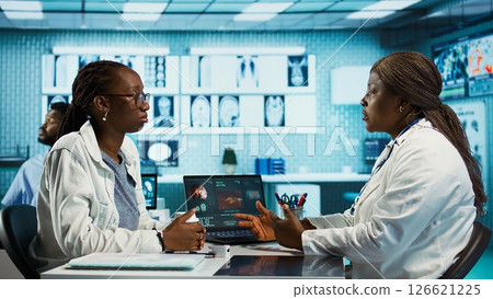 Black general practitioner explaining clinical records and results to a patient during a health care visit, focusing on treatment advice and effective communication in a facility office. Camera B. 126621225