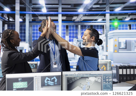 Smiling managers in photovoltaics factory doing high five, happy with performance of solar panels manufacturing. Pleased management team celebrating passing solar plant machinery inspection Smiling managers in photovoltaics factory doing high five, happy with performance of solar panels manufacturing. Pleased management team celebrating passing solar plant machinery inspection 126621325