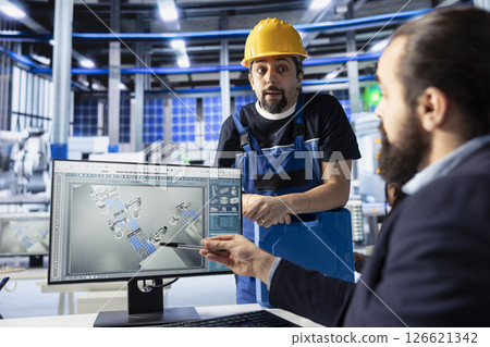 Manager in photovoltaics factory talking with worker, diagnosing malfunctioning systems, pointing to PC screen. Solar panels manufacturing plant experts doing brainstorming to reduce downtime 126621342