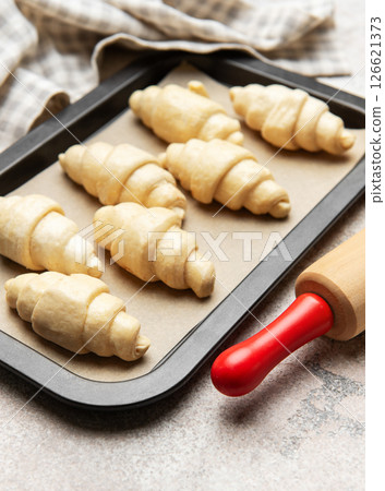 Raw croissants baking on tray with rolling pin and kitchen towel 126621373
