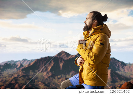 Nature lover stands at the edge of a breathtaking mountain range, looking at the scenic background of towering peaks and vast sky. Young man enjoying adventure and outdoor exploration. Nature lover stands at the edge of a breathtaking mountain range, looking at the scenic background of towering peaks and vast sky. Young man enjoying adventure and outdoor exploration. 126621402