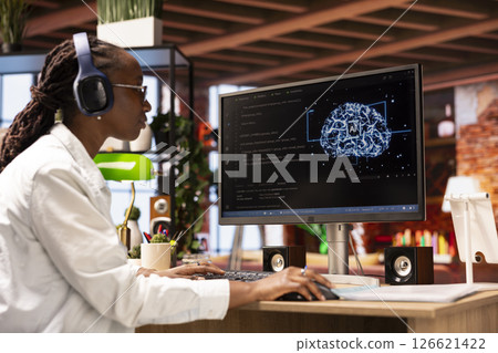 Engineer using computer at home for artificial intelligence computing through self learning algorithms, wearing headphones. Remote employee works with AI neural networks on desktop PC, listening music Engineer using computer at home for artificial intelligence computing through self learning algorithms, wearing headphones. Remote employee works with AI neural networks on desktop PC, listening music 126621422