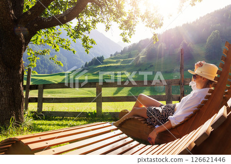 Portrait happy smiling woman sunglasses enjoy relax on wooden lounge chair outdoors in alpine countryside resort hotel garden warm sunny summer day. Alpine rural eco-tourism vacation retreat outdoors Portrait happy smiling woman sunglasses enjoy relax on wooden lounge chair outdoors in alpine countryside resort hotel garden warm sunny summer day. Alpine rural eco-tourism vacation retreat outdoors 126621446