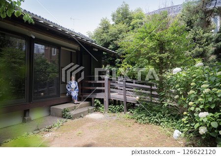 A woman in a yukata relaxing on the veranda of an old house's garden, wide-angle 126622120
