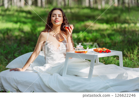 Young woman has breakfast in bed in a summer forest Young woman has breakfast in bed in a summer forest 126622246
