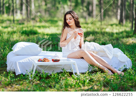 Young woman has breakfast in bed in a summer forest Young woman has breakfast in bed in a summer forest 126622255