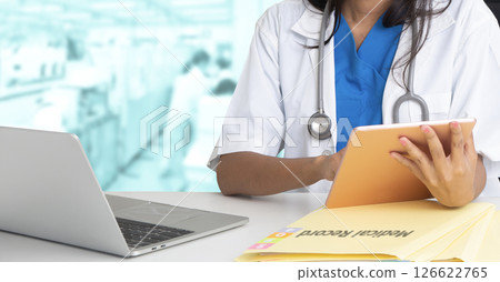Female doctor working with digital tablet and laptop at desk in hospital. 126622765