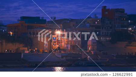 Varanasi, Uttar Pradesh, India. Old temple Sri Kumaraswami Mutt on Kshemeshvar Ghat. Evening night time. Camera moving along riverbank embankment. View from riverside. Skyline in night lights 126622991