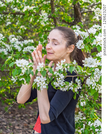 Young woman sneezes in the park against the background of a flowering tree. Allergy to pollen concept. Young woman sneezes in the park against the background of a flowering tree. Allergy to pollen concept. 126623207