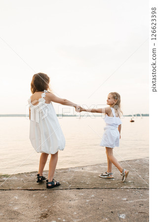 Two young girls are walking on beach, one of them holding the other's hand 126623398