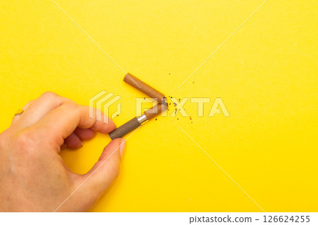 Female hand holding broken cigarette on a yellow background close up. 126624255