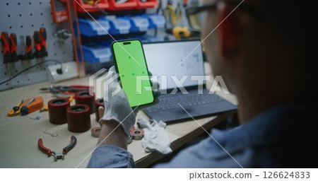 Man Checking Real-Time Stocks on Laptop and Smartphone with Green Screen Mock Up in Workshop 126624833