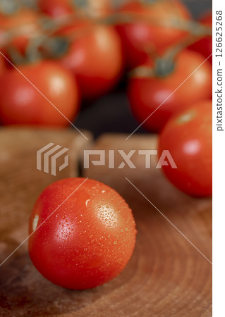 several red round cherry tomatoes on the table with small green tails 126625268
