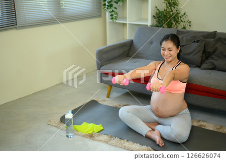 Happy pregnant woman doing light weight exercises at home on a yoga mat Happy pregnant woman doing light weight exercises at home on a yoga mat 126626074