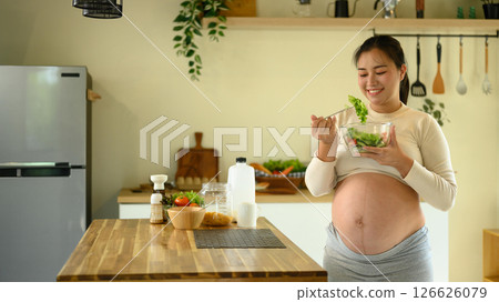 Pregnant woman enjoying a fresh salad in a modern kitchen 126626079