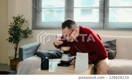 Older man in red sweater smelling coffee brewed with pour-over set on wooden table Older man in red sweater smelling coffee brewed with pour-over set on wooden table 126626210
