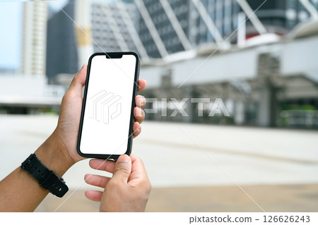 Hands holding smartphone with blank white screen in an urban cityscape 126626243