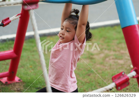 happy toddler girl hanging the bar by her hand at outdoor playground in park 126626329