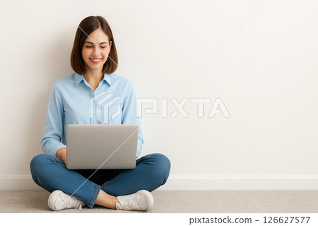 Young caucasian woman smiling while using a laptop on the floor against a minimalist white background. concept of comfortable online work, casual home style, technology interaction, copy space. 126627577