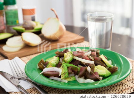 Salad of black tomatoes, avocado and onions on green plate 126628639