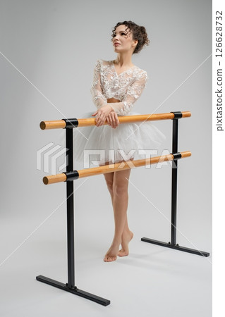 Elegant ballet dancer poses gracefully near a barre under soft lighting Elegant ballet dancer poses gracefully near a barre under soft lighting 126628732