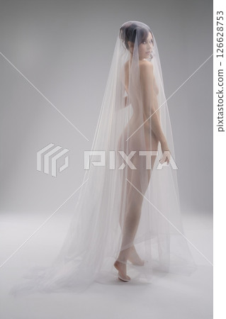 Woman dressed in sheer veil posing elegantly in a minimalist setting Woman dressed in sheer veil posing elegantly in a minimalist setting 126628753
