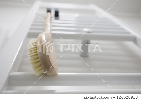 Wooden brush for dry brushing massage hanging on heated towel rail 126628918