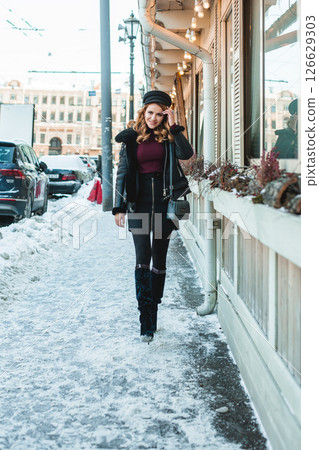 Beautiful glamorous brunette woman in black leather jacket and black hat standing 126629303