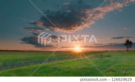 Breathtakingly stunning sunset over lush green fields, accompanied by majestic clouds above Time lapse. Breathtakingly stunning sunset over lush green fields, accompanied by majestic clouds above Time lapse. 126629629