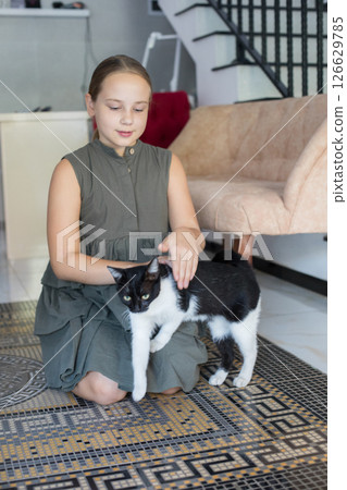 Friendly young girl hugging her cat pet sitting on floor, relaxing at home.  126629785