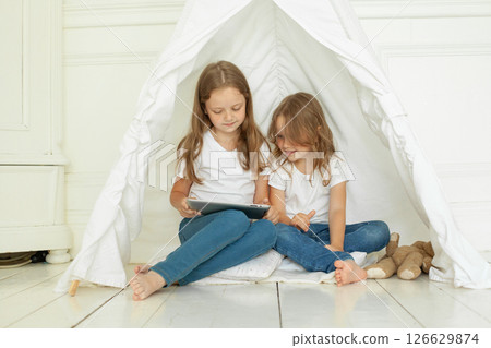 Adorable little girl sisters with tablet pc computer in kids tent at home.  126629874
